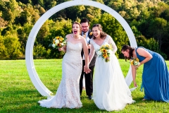 Two brides hold hands and laugh, looking back at their guests at Bellevue Farm Winery in Blacksburg, VA, during their wedding ceremony.