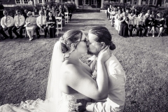 Bride and groom share a kiss as wedding guests watch from behind during their ceremony.